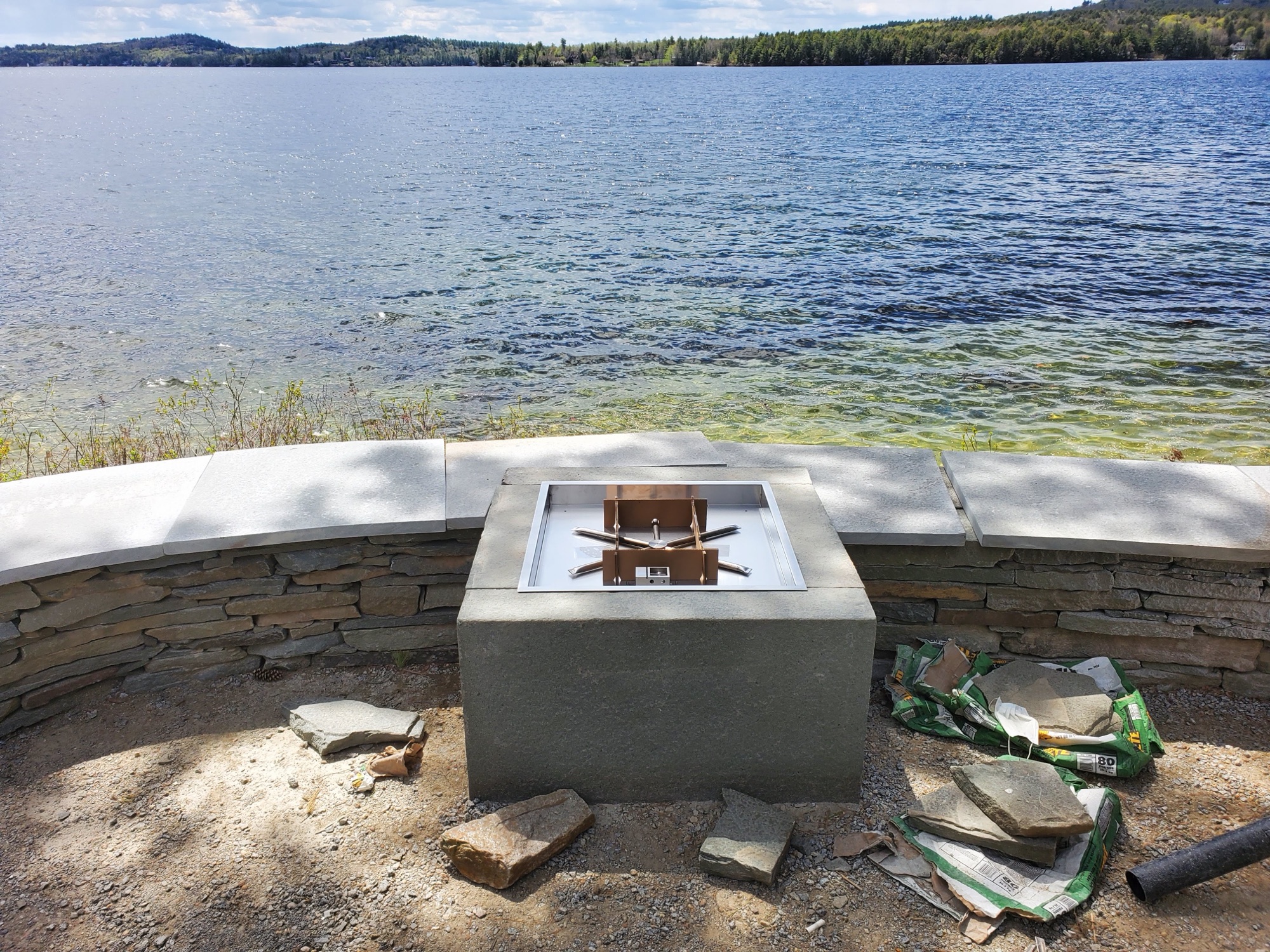 Stainless fire pit set on a stacked stone base at the edge of a lake