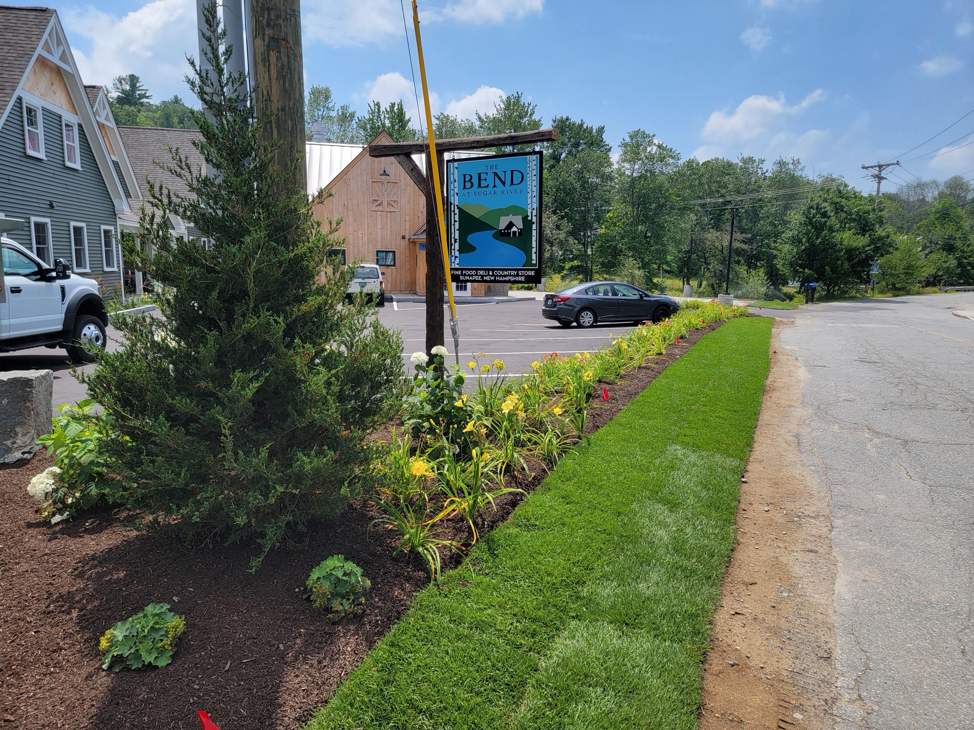 Commercial landscape with fresh sod ribbon and a mulched perennial bed along a business sign