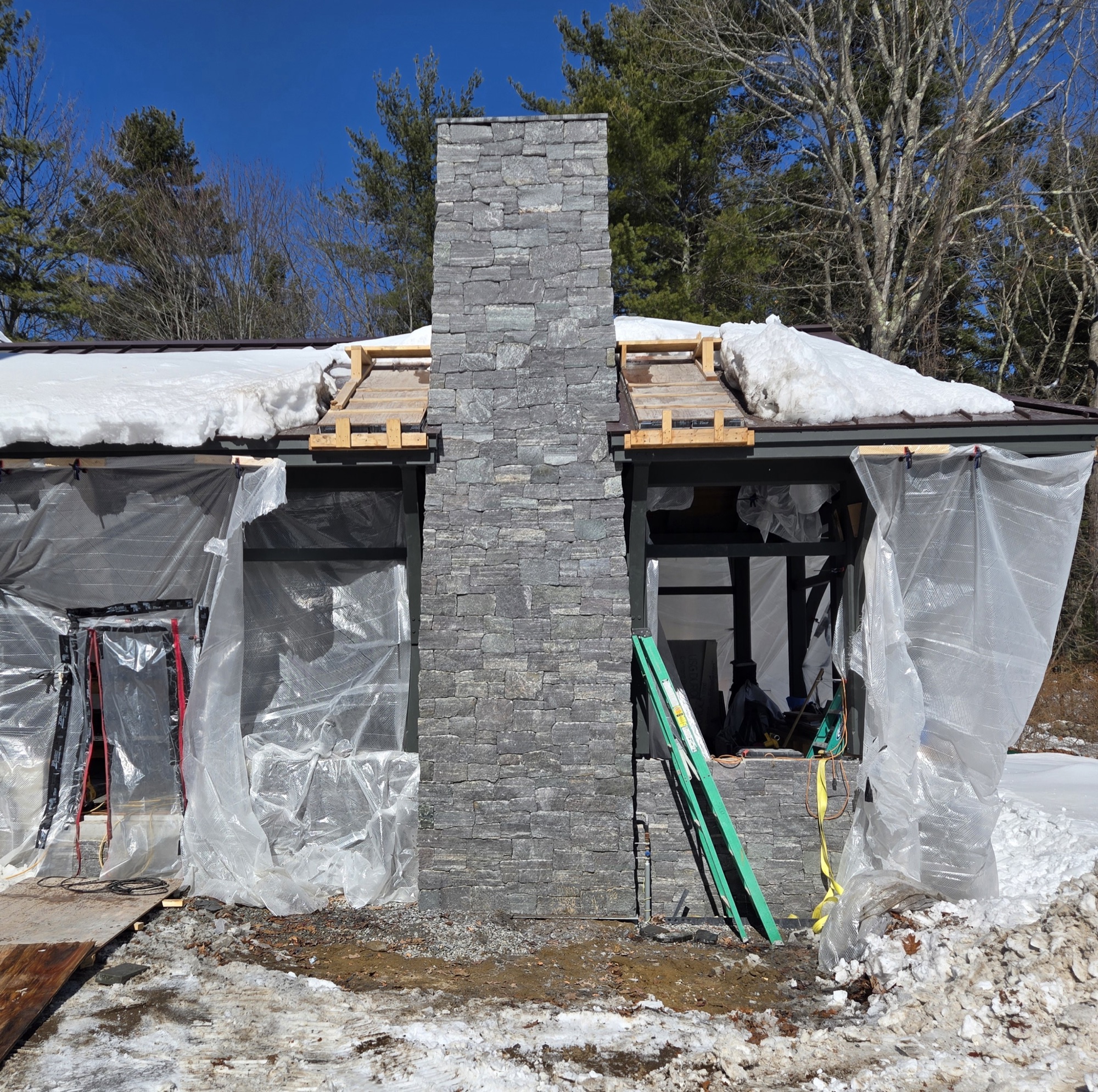 New stacked-stone chimney rising out of a home under construction