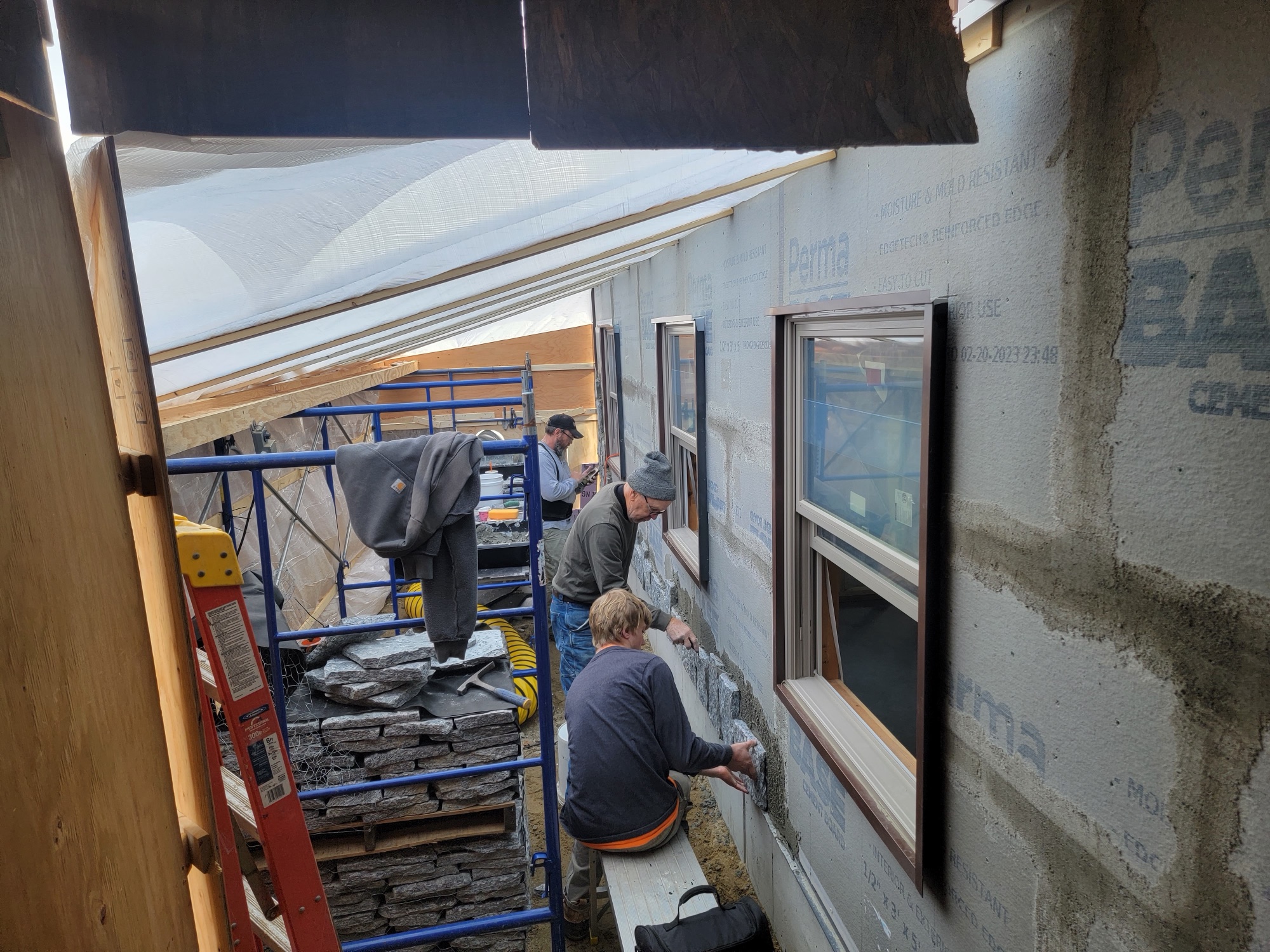 Masons installing veneer stone on a wrapped house wall