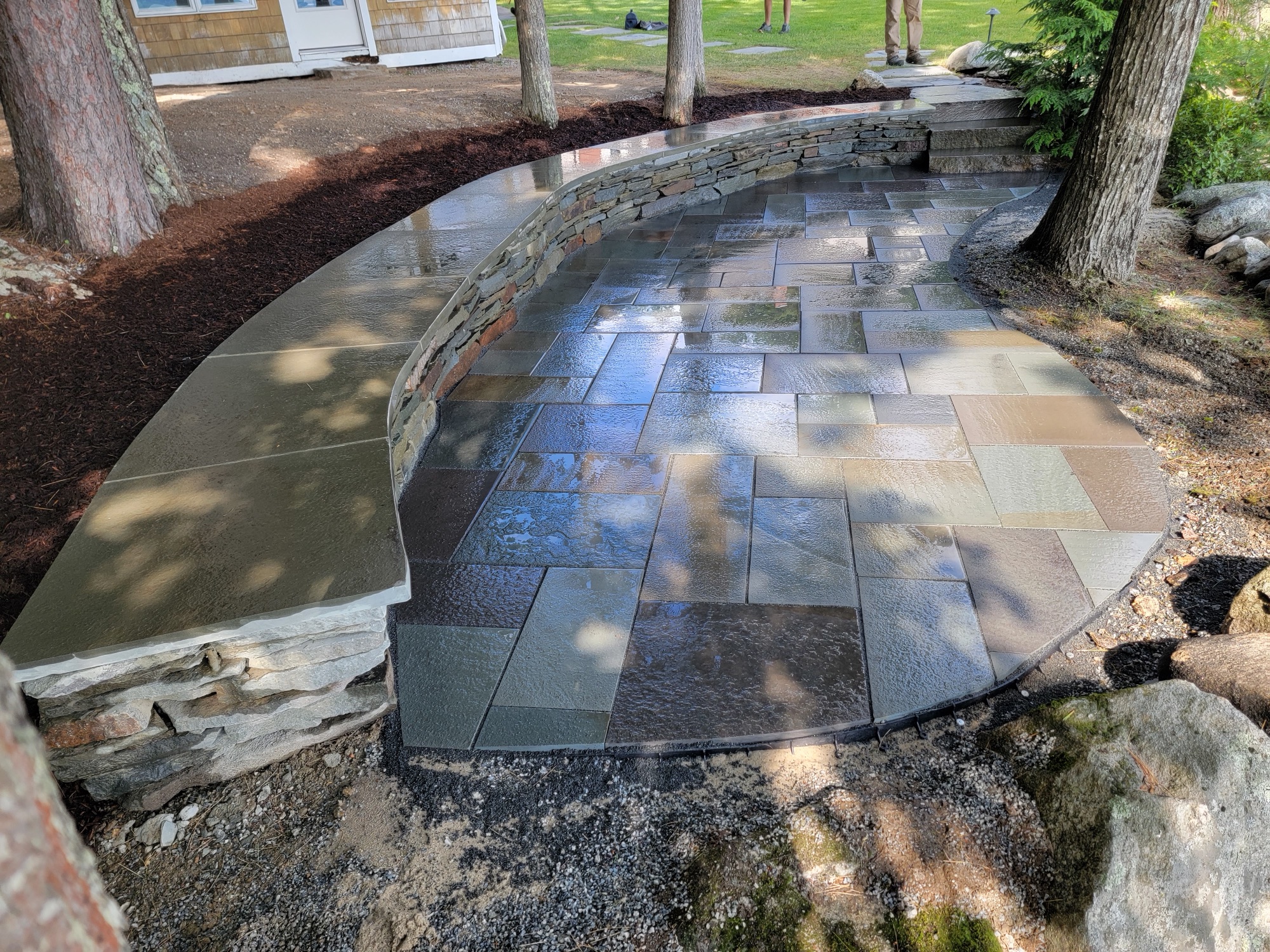Two-tier bluestone patio with stacked-stone retaining wall after rain