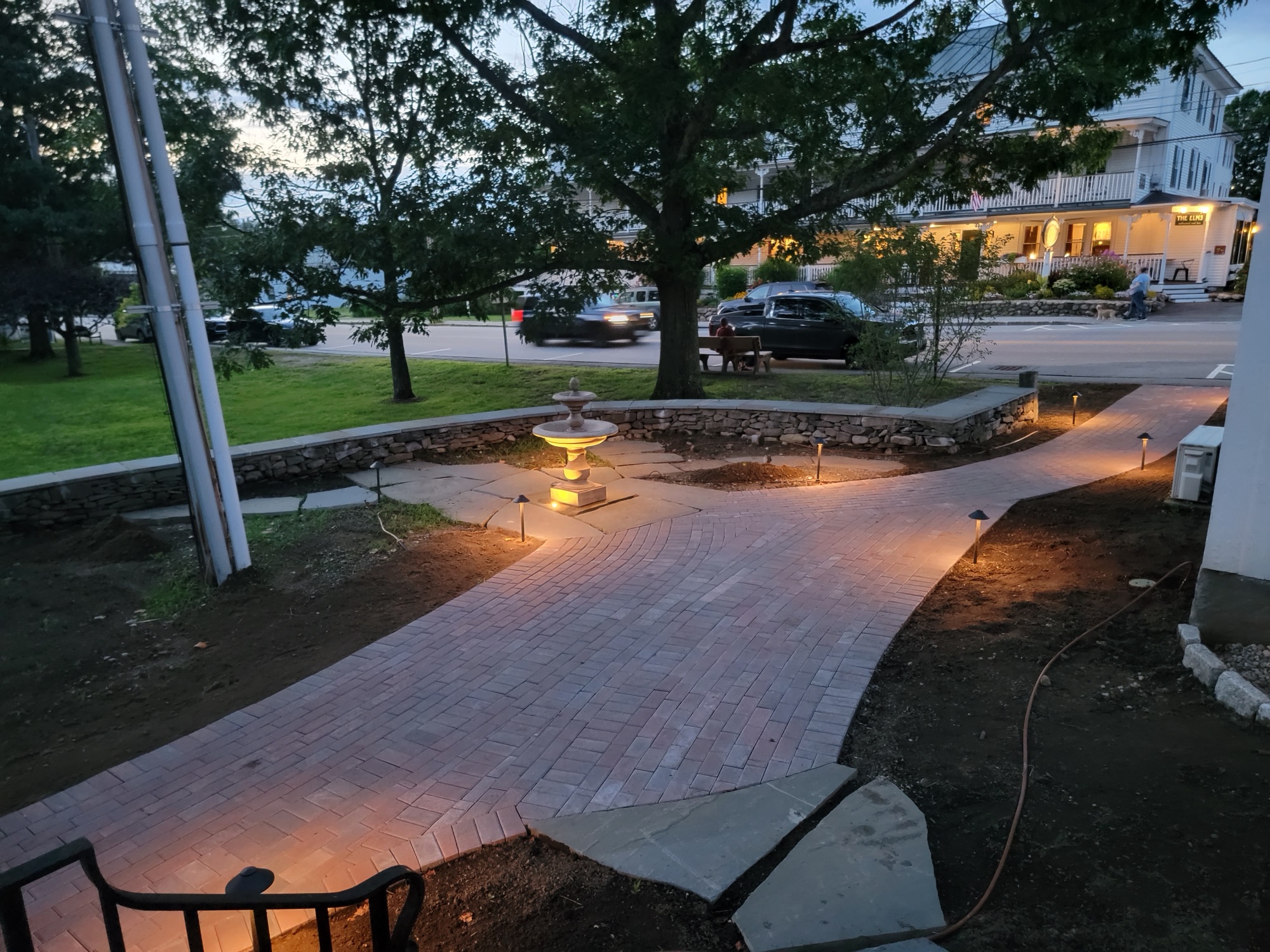 Brick paver walkway with central fountain at twilight, illuminated by path lights